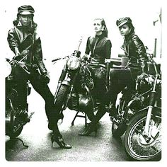 three people sitting on motorcycles in black and white with one person standing next to the motorcycle