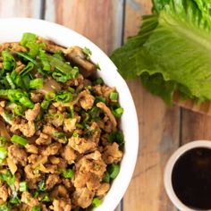 a white bowl filled with meat and green onions next to a cup of black coffee