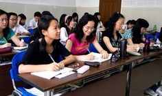 a group of people sitting at desks in a classroom with notebooks and pens