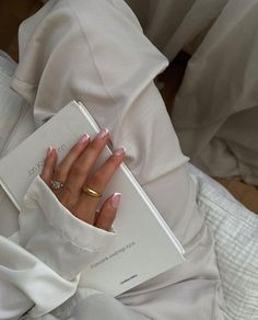 a woman's hand holding a book in her lap while wearing a white dress