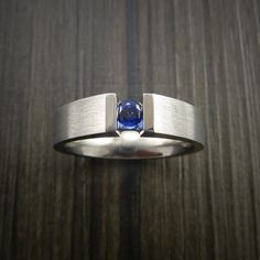 This Titanium Band Features: - 5mm Width- Flat Ring Shape- Satin Finish- Faux Tension Set .16ct (3.5mm) Sapphire. The stone is held firmly between Cathedral arms. Modern Channel Set Promise Rings, Minimalist Sapphire Ring With Tension Setting For Formal Occasions, Minimalist Sapphire Ring With Tension Setting, Elegant Titanium Ring Jewelry, Elegant Titanium Ring, Modern Round Sapphire Ring For Formal Occasions, Modern Sapphire Ring For Formal Occasions, Elegant Silver Titanium Ring, Elegant Titanium Rings For Formal Occasions