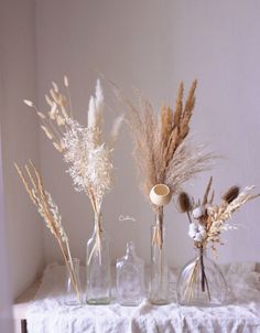 three vases filled with dried plants on top of a white cloth covered tablecloth