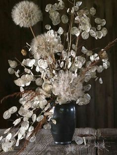 a vase filled with lots of white flowers on top of a wooden table next to a wall