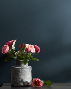 some pink roses are in a gray vase on a table next to a black wall