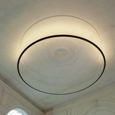 a circular light fixture hanging from the ceiling in a room with white walls and arched windows