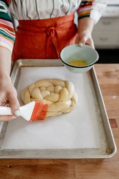 a woman in an apron is spreading icing onto some bread on a baking sheet