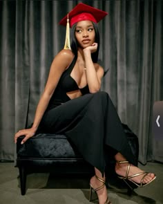 a woman in a graduation cap and gown sitting on a chair with her hand under her chin