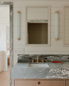 a bathroom with marble counter tops and gold faucets on the sink, along with white walls