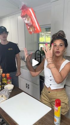 a woman standing in front of a kitchen counter holding her hands up to the camera