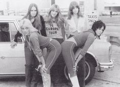 four women are posing in front of a car