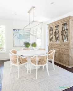 a dining room table and chairs in front of a china cabinet with a painting on the wall