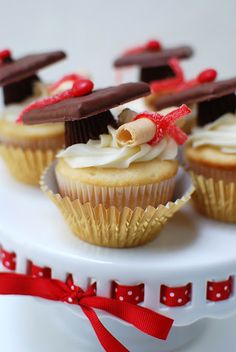 cupcakes decorated with graduation hats and red ribbons on a white cake platter