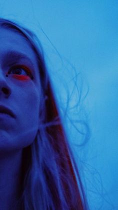 a woman with long hair and red eyes stares into the distance while standing in front of a blue sky