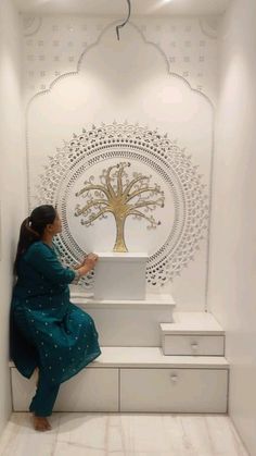 a woman sitting on top of a white bench in front of a wall with a tree