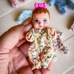 a hand holding a tiny doll with blue eyes and a pink bow on her head