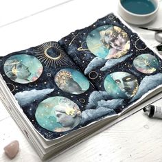 an open book with pictures of the moon and stars on it, sitting next to a cup of coffee