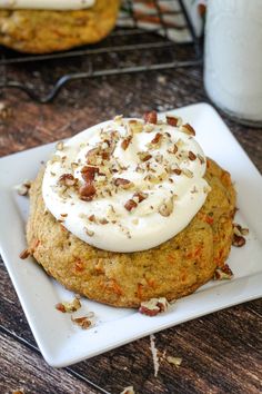 two cookies with white frosting and chopped pecans on a plate next to a glass of milk