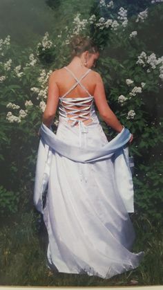 a woman in a white dress is walking through the grass with flowers on either side