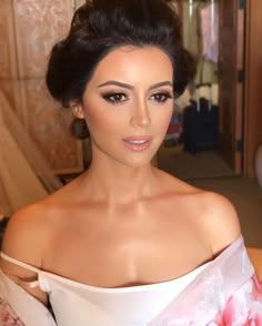 a woman with dark hair wearing a white dress and pink flowered shawl, posing for the camera