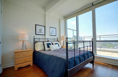 a bedroom with a bed, nightstands and large windows overlooking the cityscape