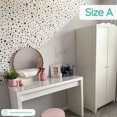 a white desk with a mirror on it next to a wallpapered background and a pink stool