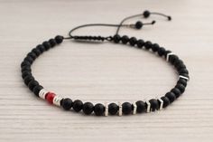 An asymmetric men's bracelet with black onyx stones, sterling silver spacers, and one red coral bead. The bracelet has one red coral bead as a focal point, adding a vibrant pop of color. It's a unique and bold accessory that combines contrasting elements, making a statement and adding individuality and style to any outfit. Details: 4mm matte black onyx 4mm red coral sterling silver spacers nylon cord Modern Black Bracelets With Gemstone Beads, Minimalist Black Bracelets With Spacer Beads, Modern Beaded Bracelet With Black Beads As Gift, Modern Gemstone Beads Bracelets, Modern Adjustable Onyx Bracelet, Modern Onyx Bracelets For Gifts, Modern Onyx Bracelets For Gift, Modern Onyx Bracelets As Gift, Modern Handmade Black Bracelets