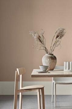 a vase with some flowers in it sitting on a table next to two white chairs