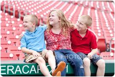 three children sitting on the bleachers at a baseball game