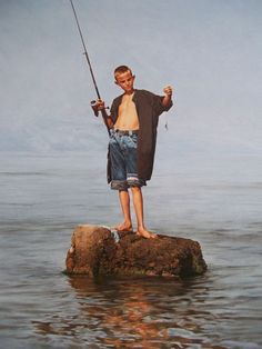 a boy is standing on a rock while holding a fishing rod