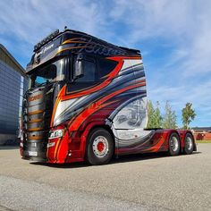 a red and black semi truck parked in front of a building with a sky background