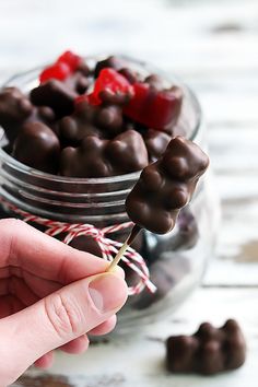 a hand holding a candy stick over a jar filled with chocolate candies