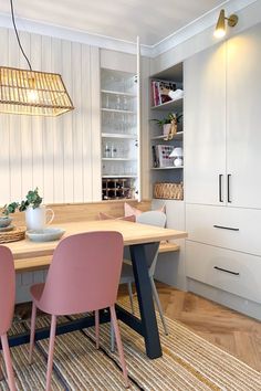 a dining room table with pink chairs in front of white cupboards and open shelves