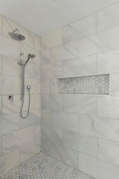 a shower with white marble tile and hexagonal tiles on the walls, along with a hand held shower head