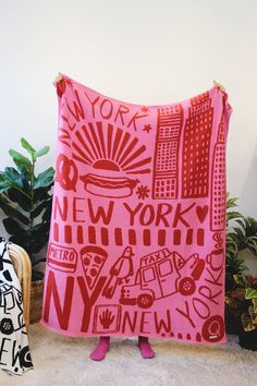 a pink blanket with new york on it sitting next to some plants and potted plants