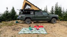 two children sitting on a blanket in front of a truck with a tent attached to it