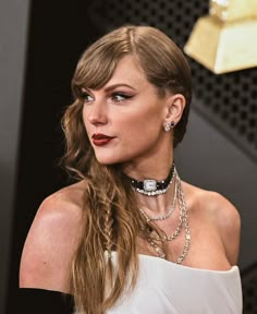 a woman with long hair wearing a white dress and jewelry on the red carpet at an event