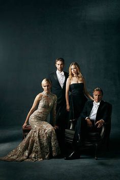 three people are posing for a photo in formal wear and tuxedo, with one woman sitting on a chair