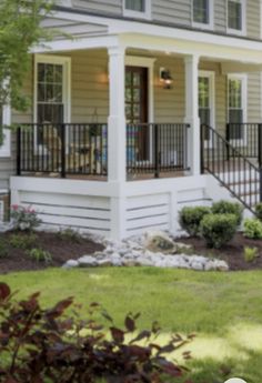 a small house with two porches on the front and second story, surrounded by landscaping