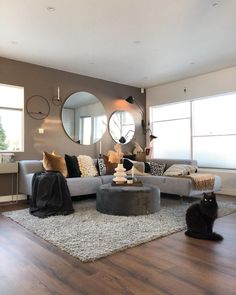 a cat sitting on the floor in front of a living room with couches and round mirrors