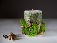 a candle that is sitting next to some moss and pinecones on a table