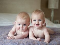 two baby babies laying on a bed with their heads turned to look at the camera