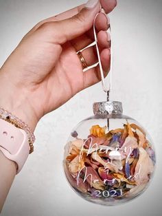 a hand holding a glass ornament with flowers in it that says hello december