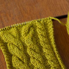 a close up of a knitted piece of cloth with yarn next to it on a wooden surface