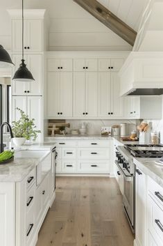 a large kitchen with white cabinets and wood flooring, along with black pendant lights