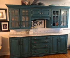 a kitchen with green cabinets and marble counter tops, framed pictures on the wall above it