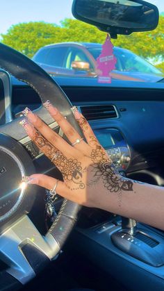 a woman's hand on the steering wheel of a car with henna tattoos