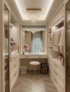 a walk - in closet with white drawers and wooden flooring is lit by a crystal chandelier hanging from the ceiling