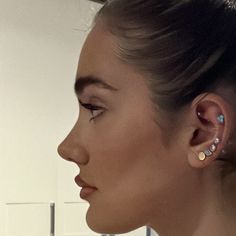 a woman with ear piercings on her ears looking off to the side in front of a mirror