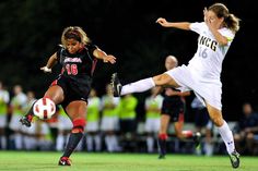 two women playing soccer on a field with people watching