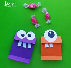 two paper bags with candy in them on a green surface, one is purple and the other is orange